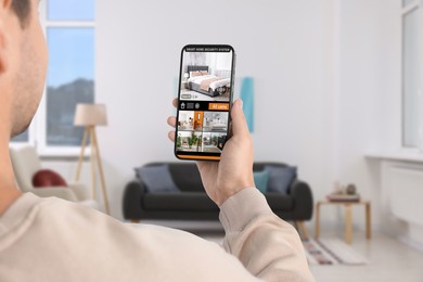 Man using smart home security system on mobile phone indoors, closeup. Device showing different rooms through cameras