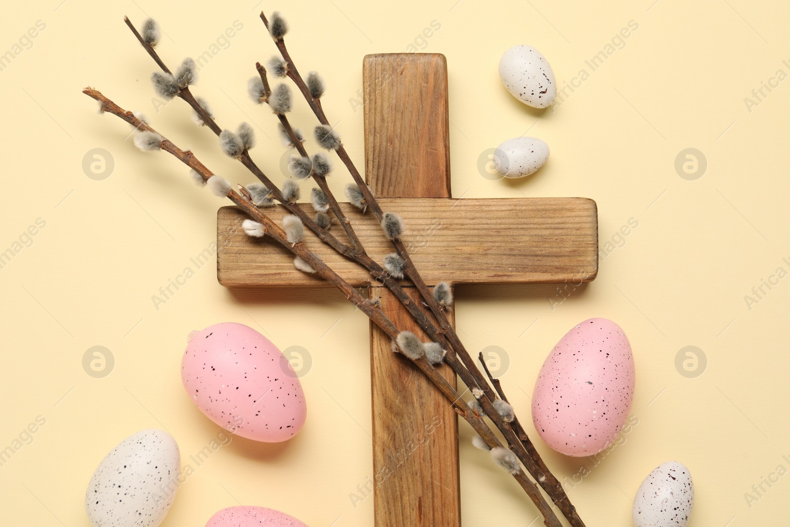 Photo of Wooden cross, painted Easter eggs and willow branches on beige background, flat lay