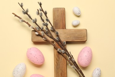 Wooden cross, painted Easter eggs and willow branches on beige background, flat lay