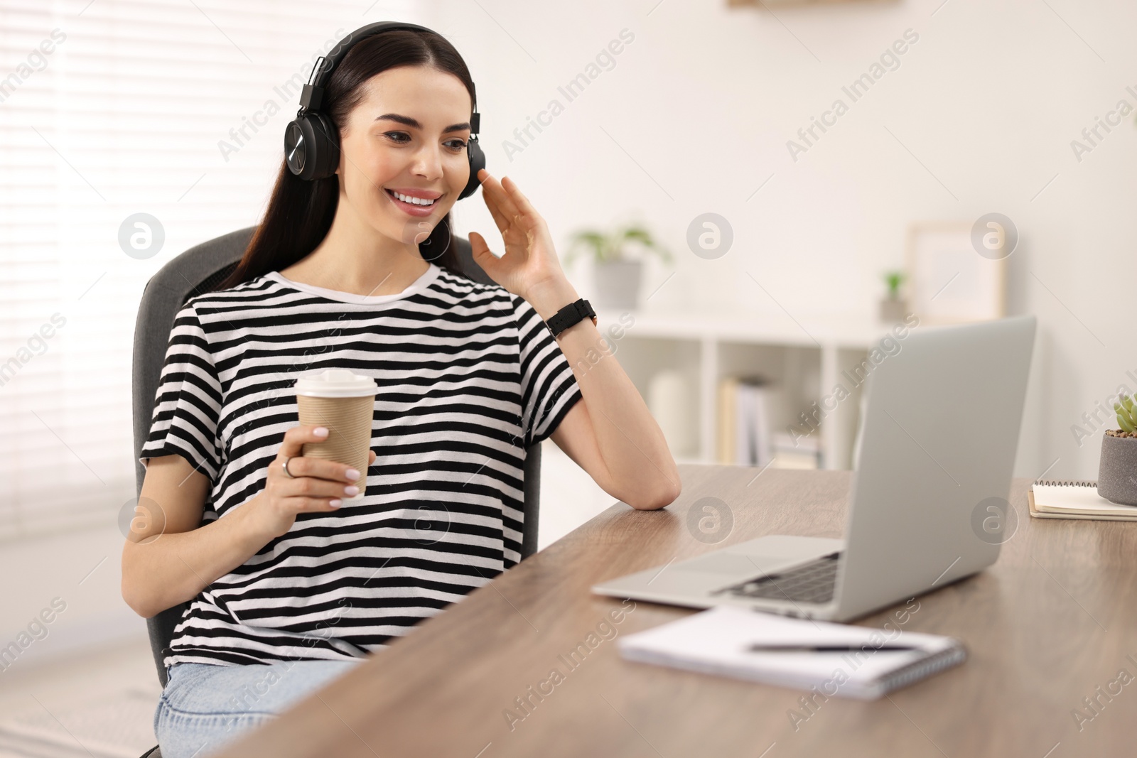 Photo of Young woman in headphones watching webinar at table in room