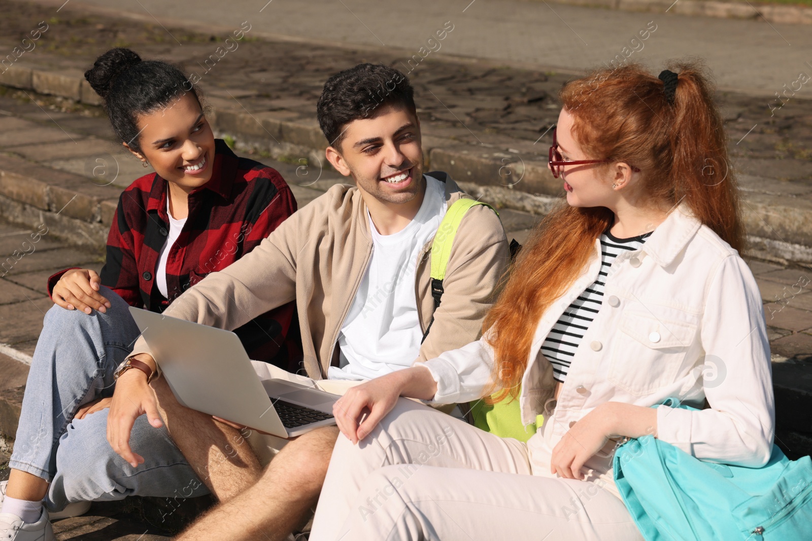 Photo of Happy young students studying with laptop together on steps outdoors
