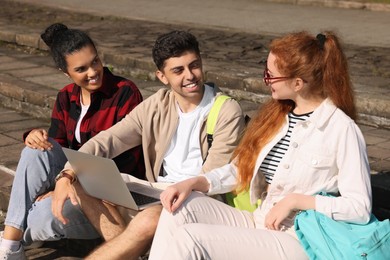 Photo of Happy young students studying with laptop together on steps outdoors