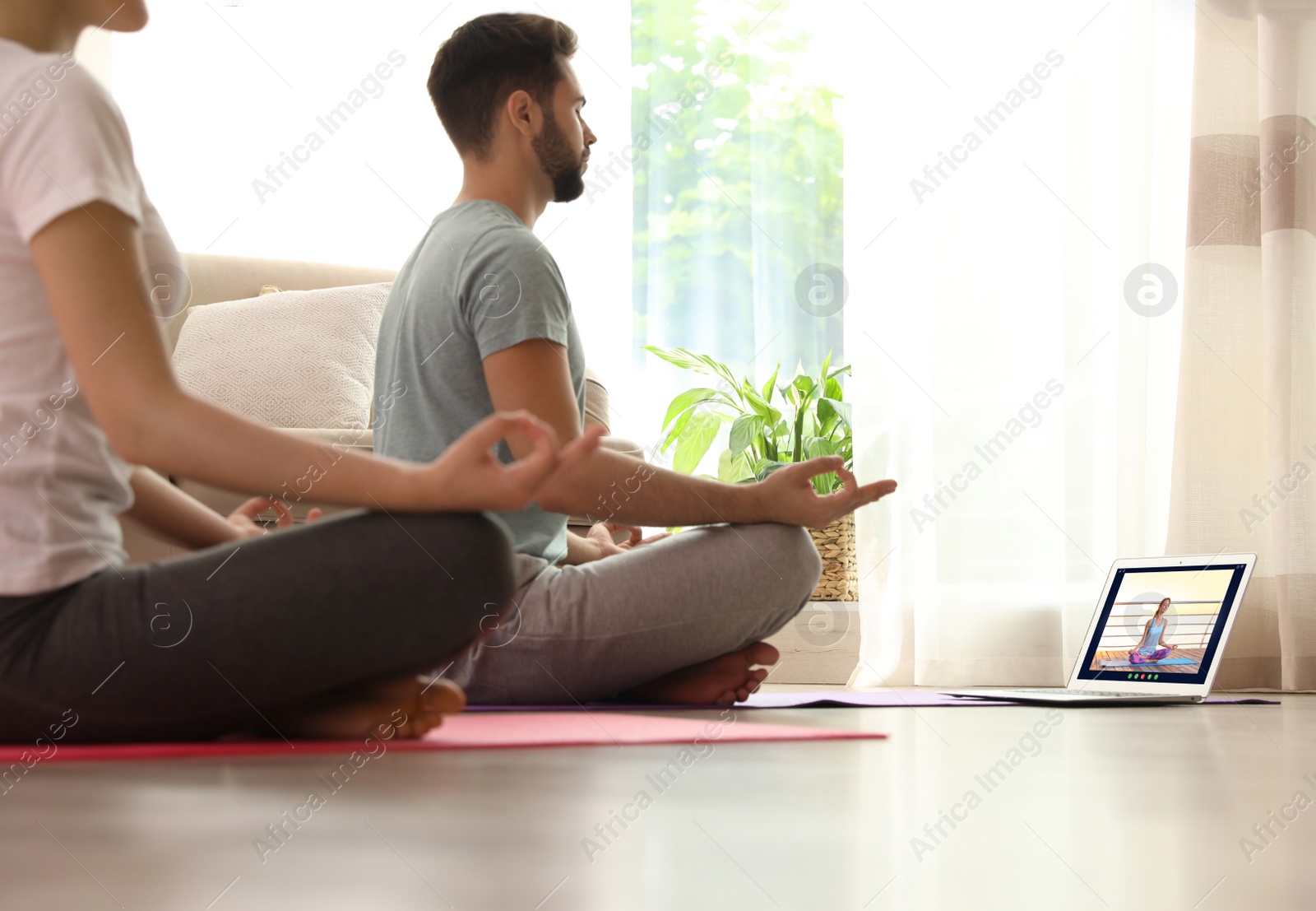Image of Distance yoga course during coronavirus pandemic. Couple having online practice with instructor via laptop at home