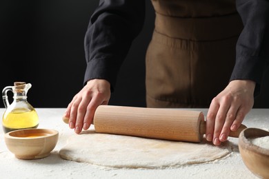 Woman rolling raw dough at table, closeup