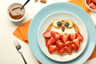 Photo of Creative serving for kids. Plate with cute owl made of pancakes, strawberries, cream, banana and almond on white wooden table, flat lay