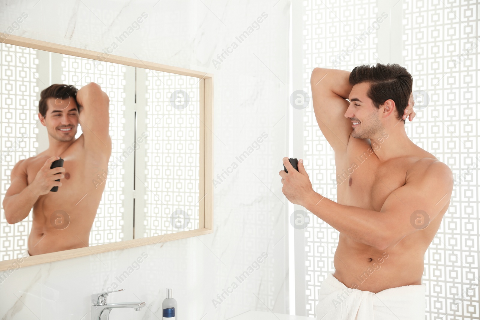 Photo of Handsome young man applying deodorant in bathroom