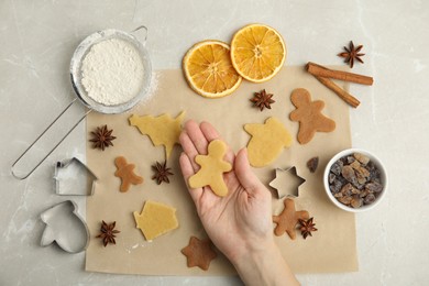 Photo of Woman holding unbaked cookie on light table, top view. Christmas biscuits