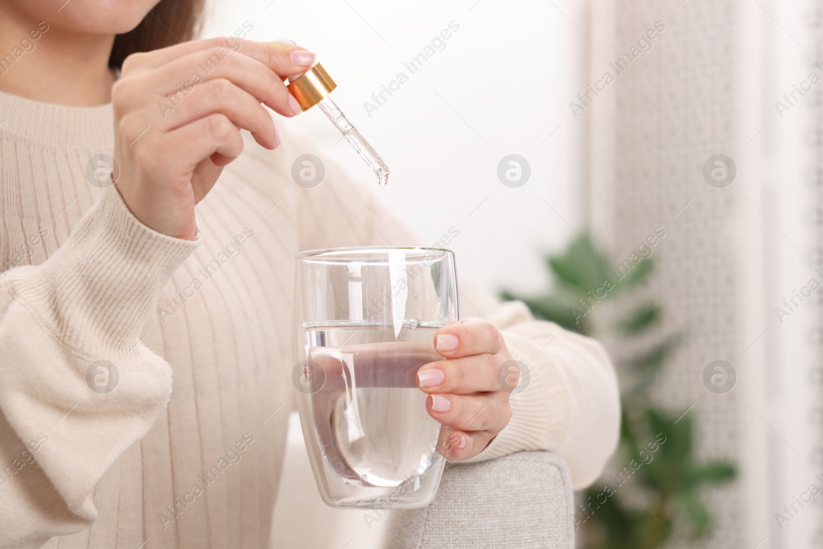 Photo of Woman dripping food supplement into glass of water indoors, closeup. Space for text