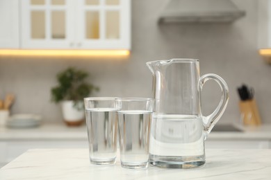 Jug and glasses with clear water on white table in kitchen