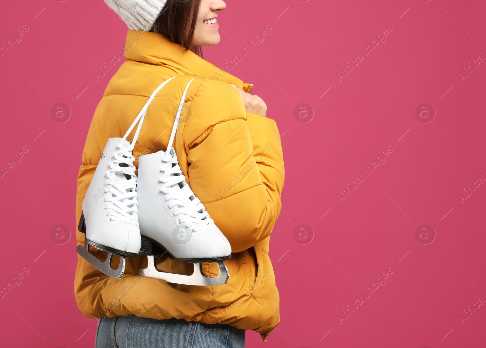 Photo of Happy woman with ice skates on pink background, closeup. Space for text