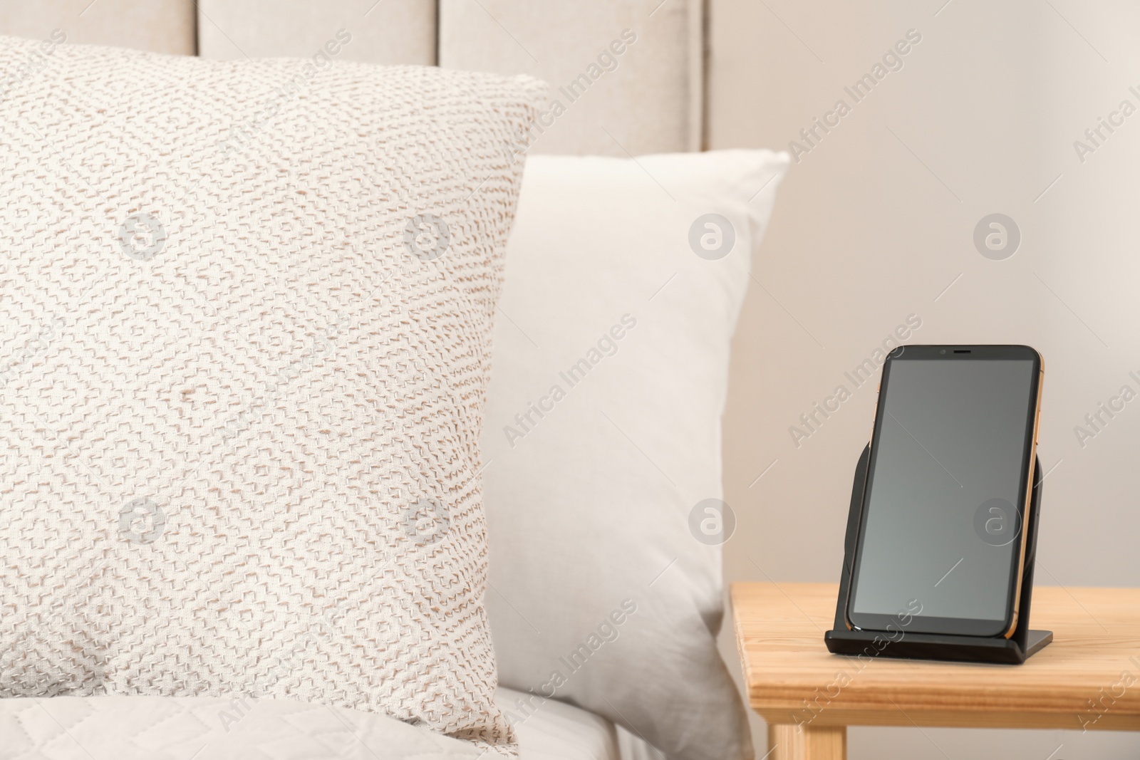 Photo of Modern mobile phone charging on wireless pad in bedroom