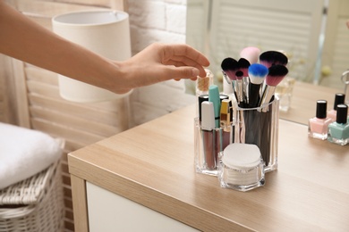 Photo of Woman taking brush from organizer for makeup cosmetic products on table