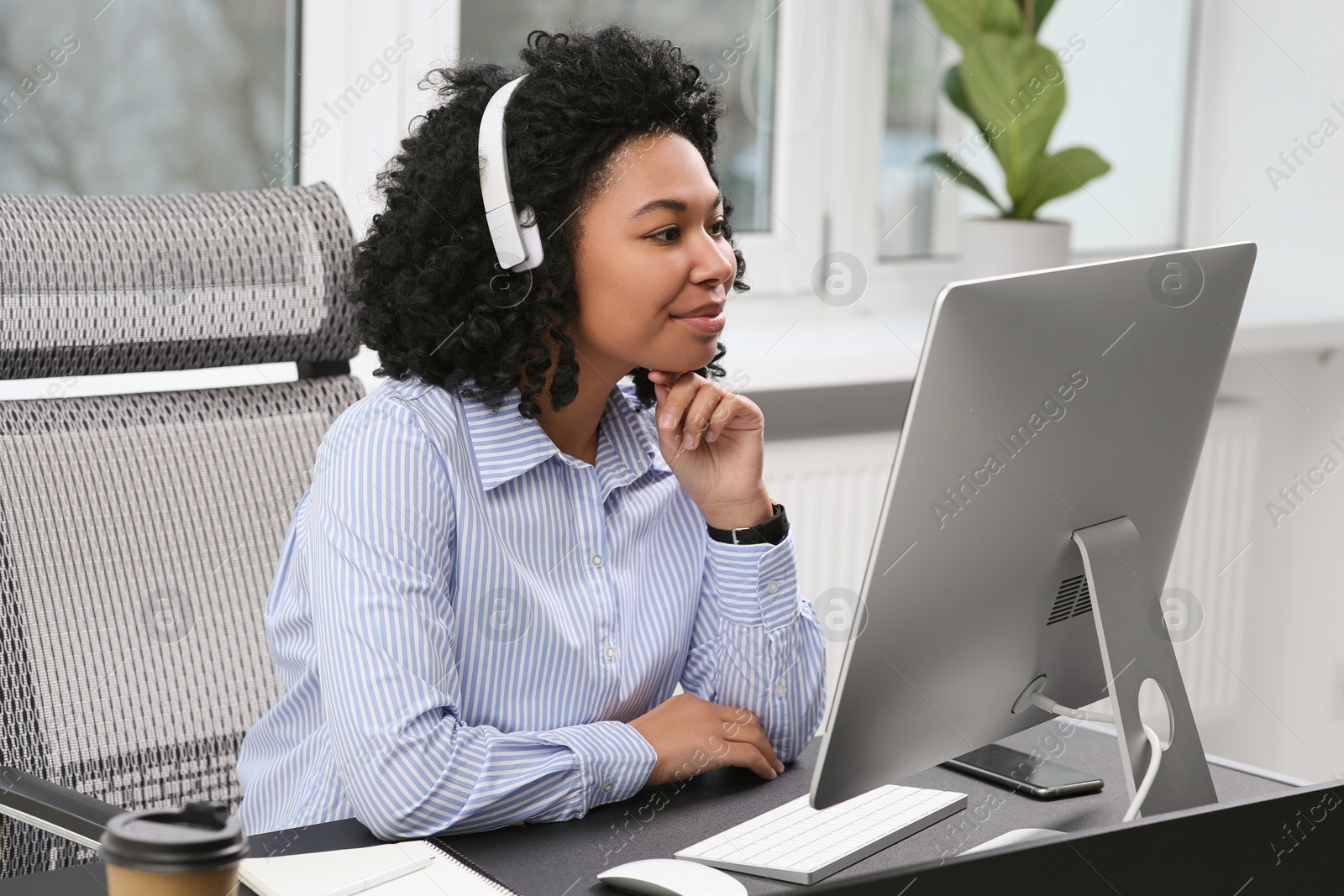 Photo of Young woman with headphones working on computer in office