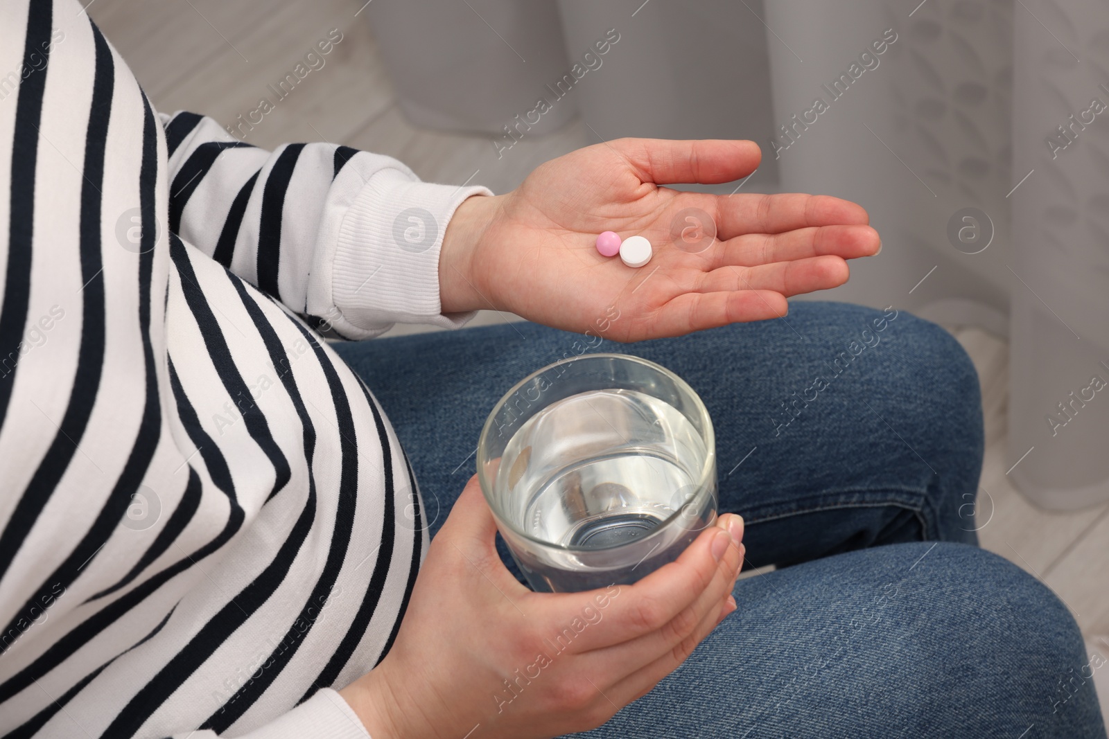 Photo of Pregnant woman with glass of water and pill at home, closeup