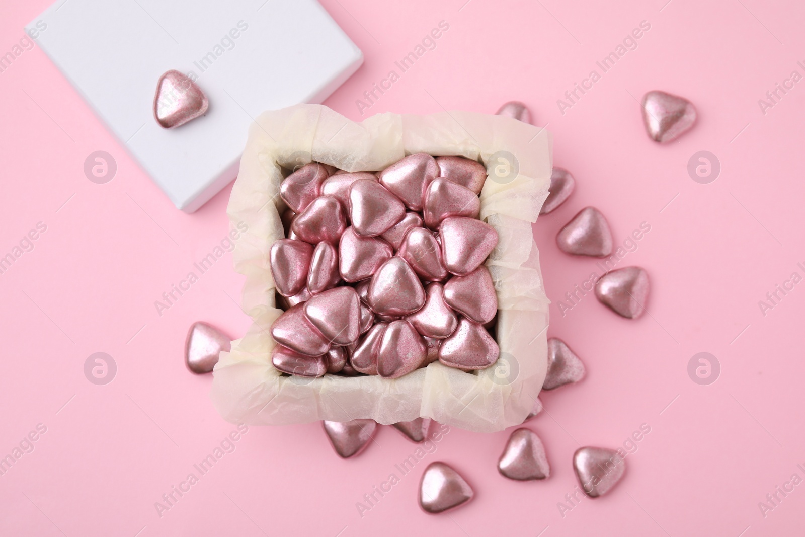 Photo of Box and delicious heart shaped candies on pink background, flat lay