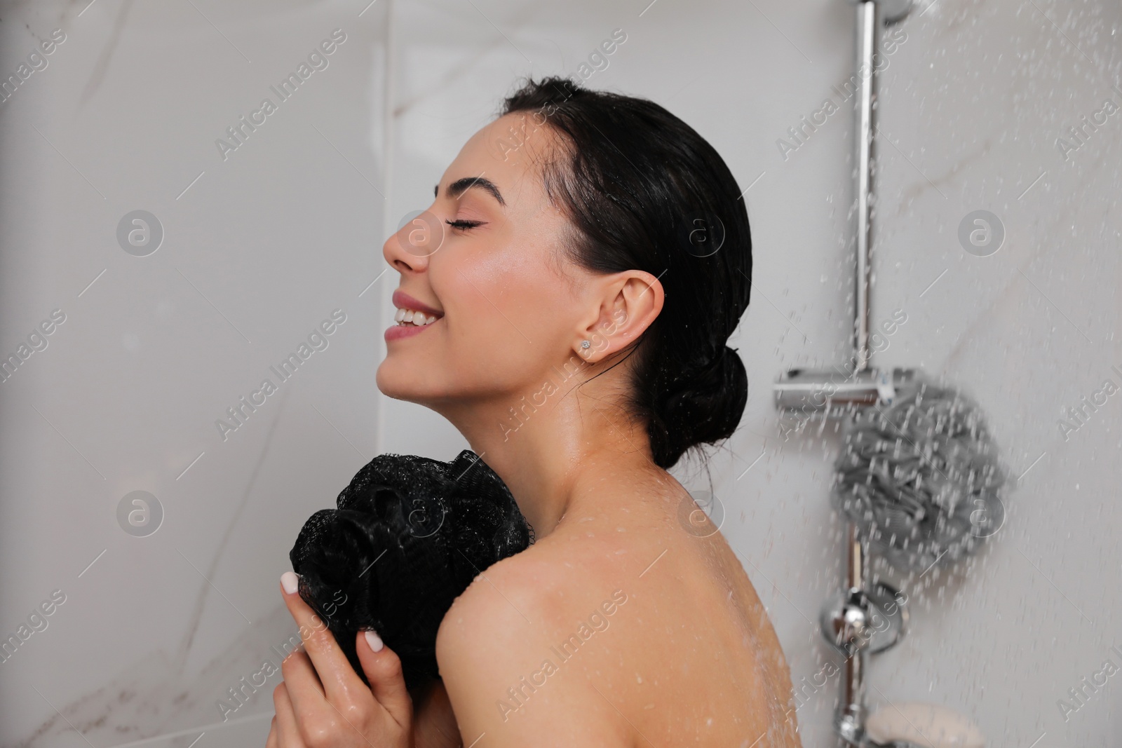 Photo of Young woman with mesh pouf taking shower at home