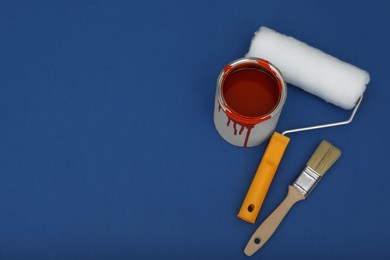Photo of Can of orange paint, roller and brush on blue background, flat lay. Space for text
