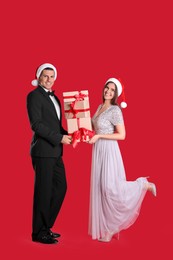 Beautiful happy couple in Santa hats holding Christmas gifts on red background
