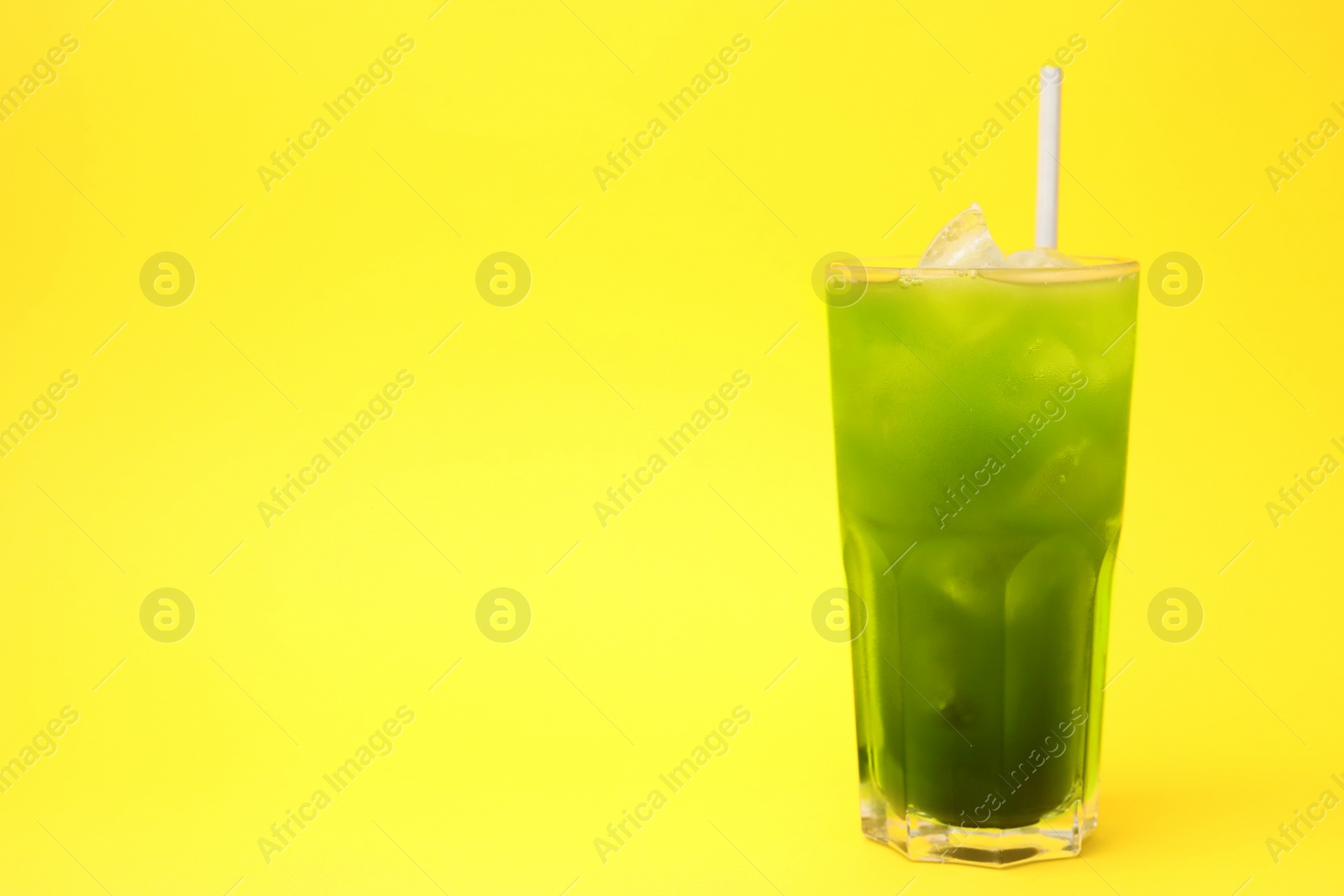 Photo of Glass of delicious iced green matcha tea on yellow background, space for text