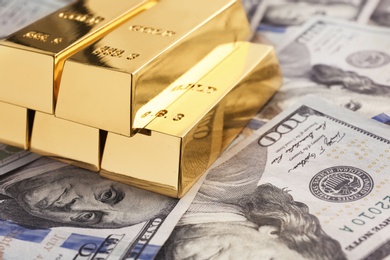 Photo of Shiny gold bars on pile of dollar bills