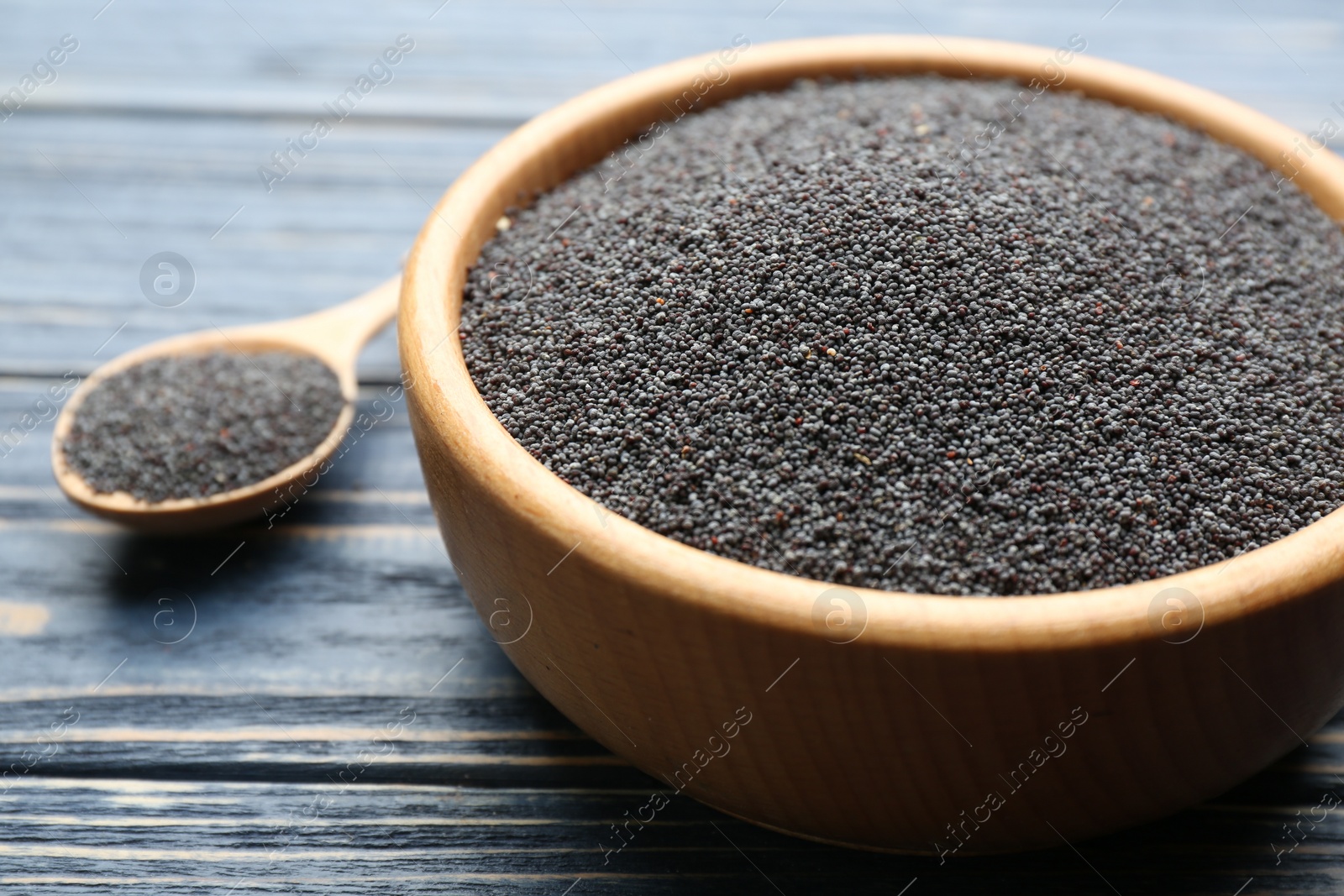 Photo of Poppy seeds in bowl on blue wooden table, closeup