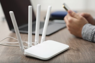 Man with smartphone and laptop working at wooden table, focus on Wi-Fi router