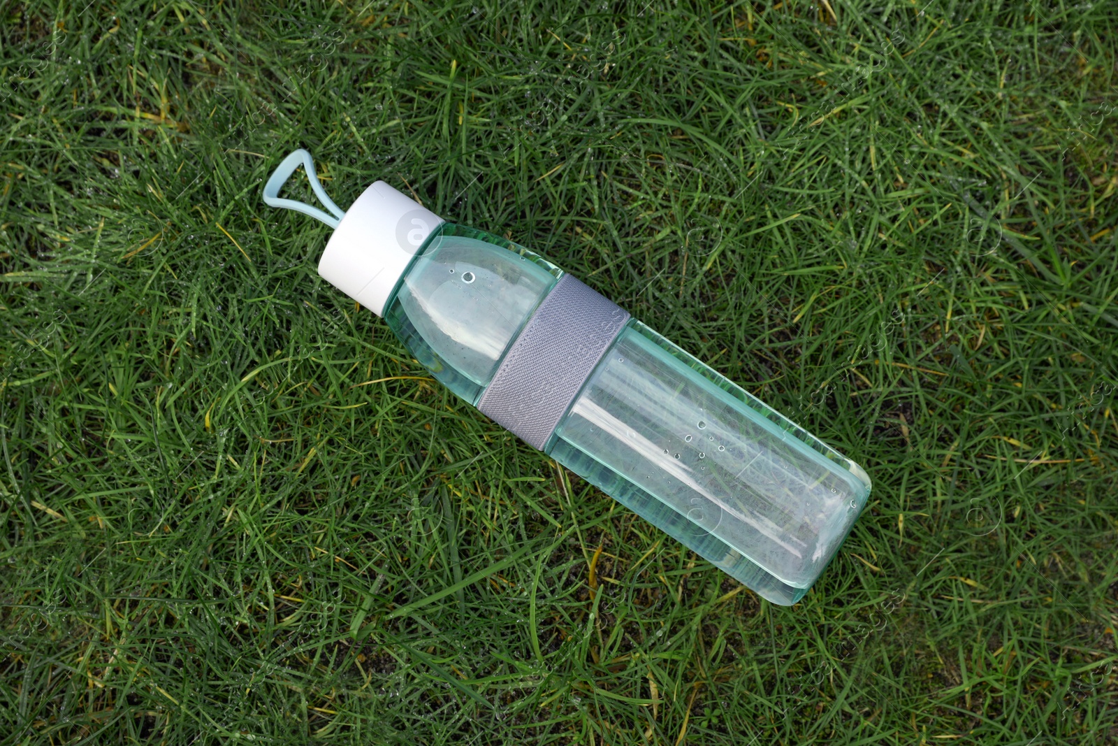 Photo of Bottle of water on green grass, top view. Morning exercise