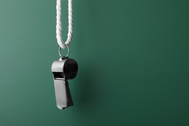 Referee equipment. Metal whistle on dark green background, closeup and space for text