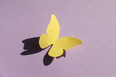 Yellow paper butterfly on violet background, top view