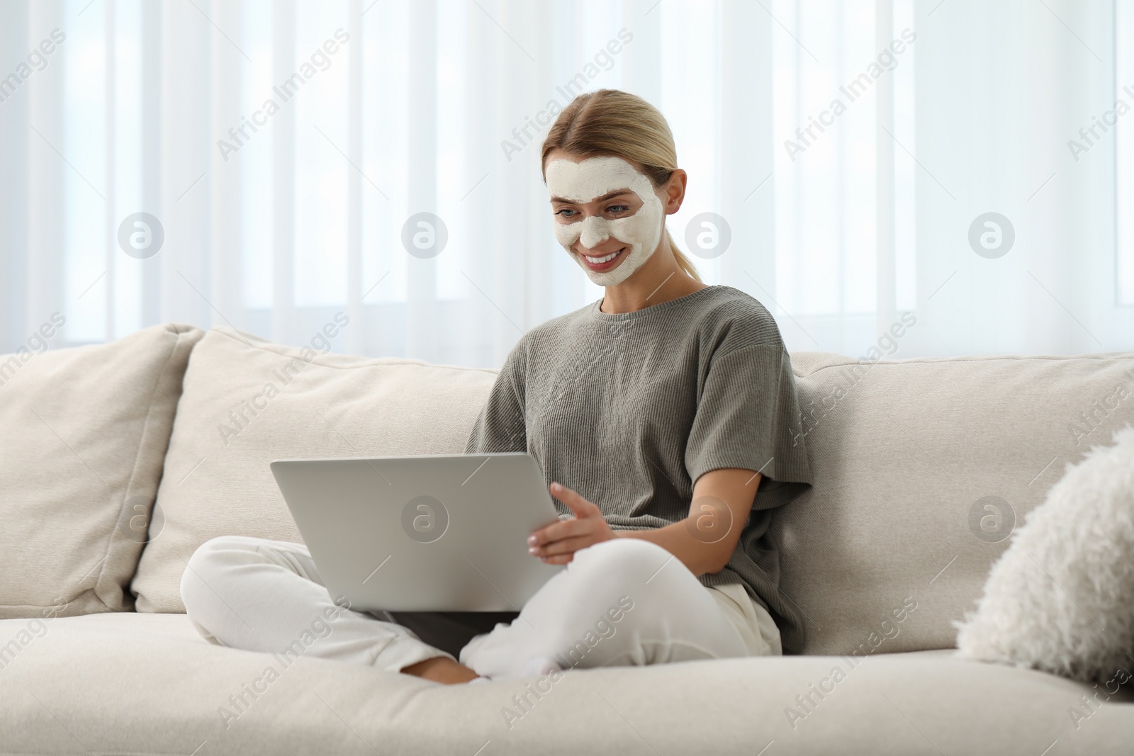 Photo of Young woman with face mask using laptop on sofa at home. Spa treatments