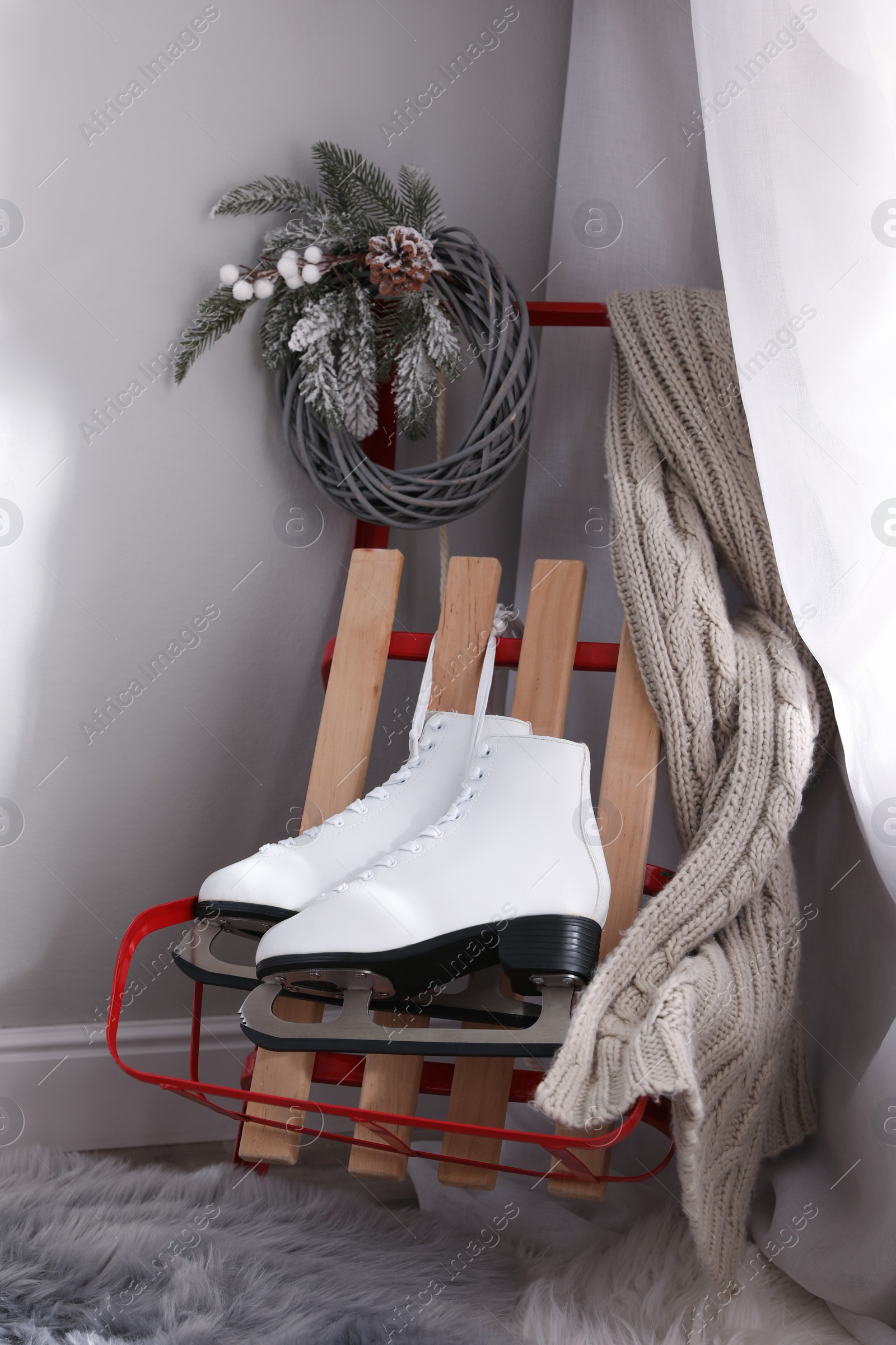 Photo of Pair of ice skates, sleigh and beautiful Christmas decor near white wall indoors