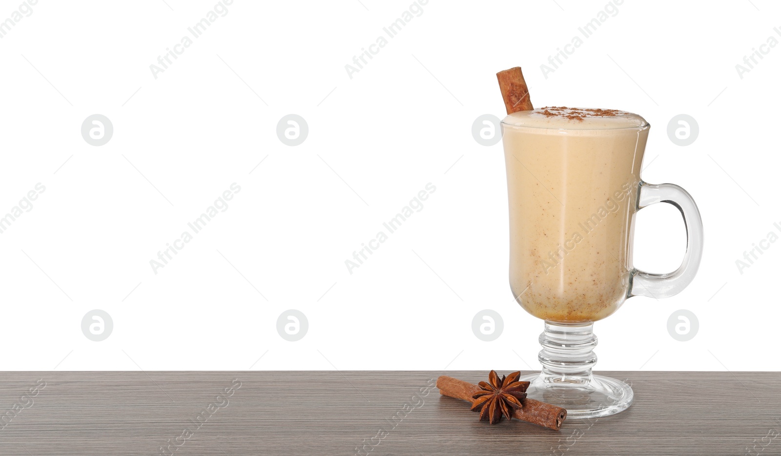 Photo of Delicious eggnog in glass, anise and cinnamon sticks on wooden table against white background, space for text