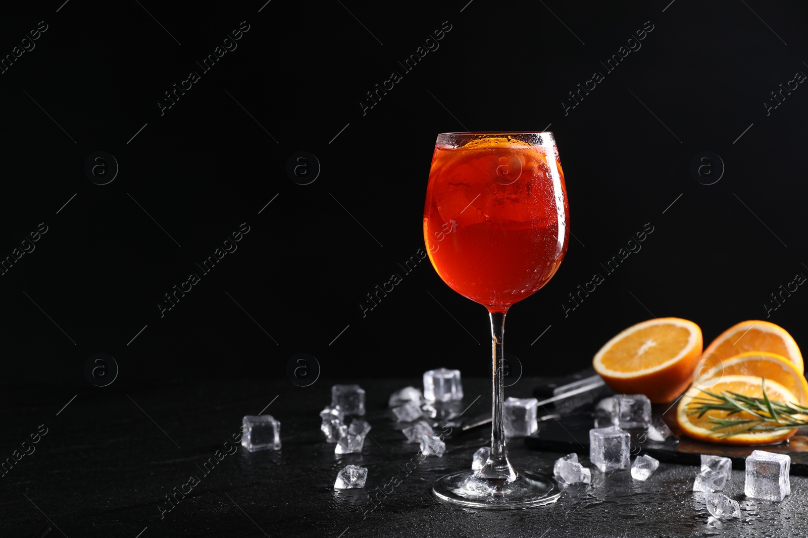 Photo of Glass of tasty Aperol spritz cocktail with orange slices and ice cubes on table against black background, space for text