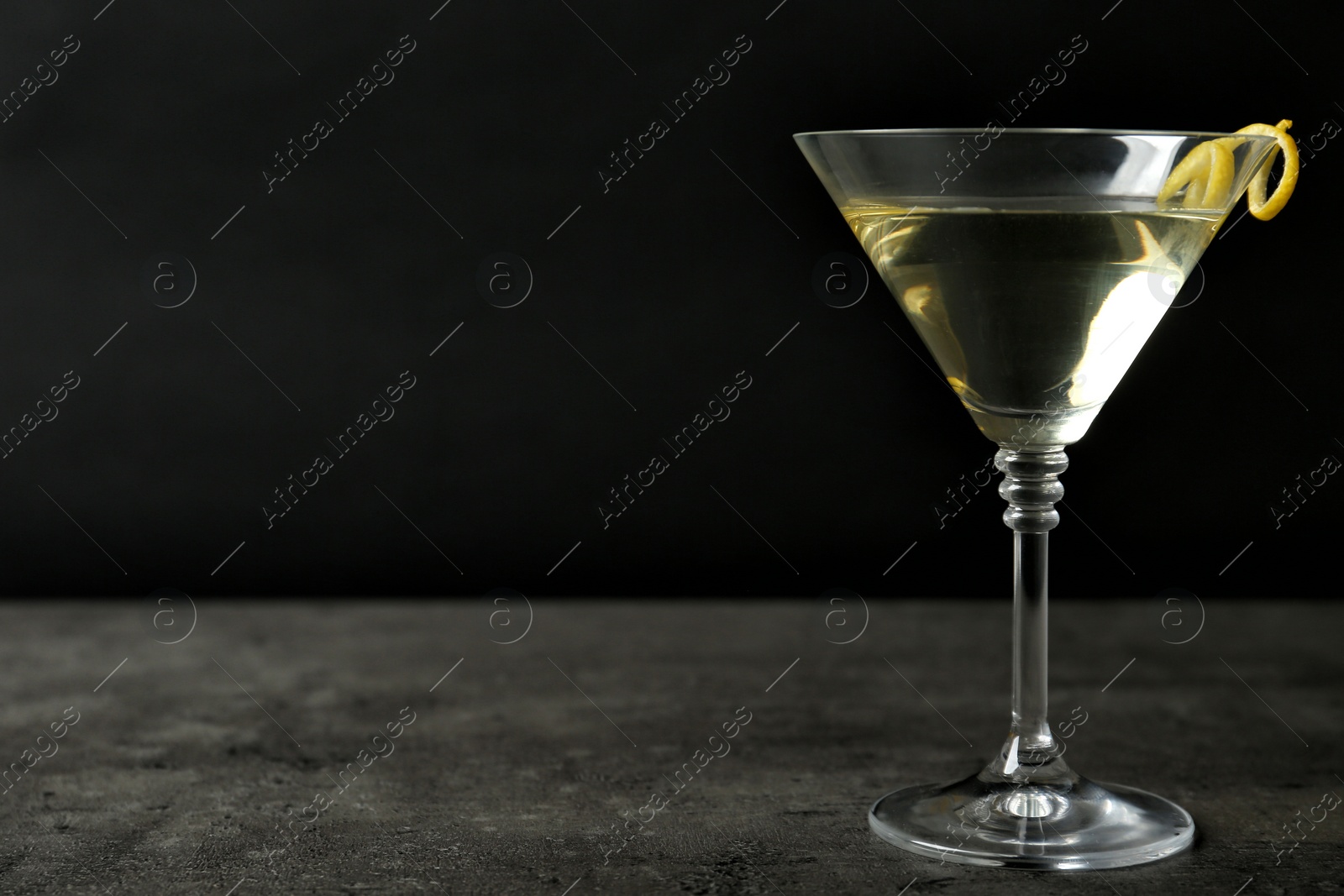 Photo of Glass of lemon drop martini cocktail with zest on stone table against black background. Space for text