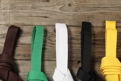 Photo of Colorful karate belts on wooden background, flat lay