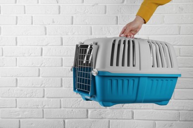 Photo of Woman holding light blue pet carrier near white brick wall, closeup. Space for text