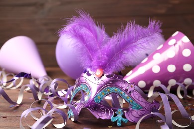 Photo of Beautiful purple carnival mask and  decor on wooden table, closeup