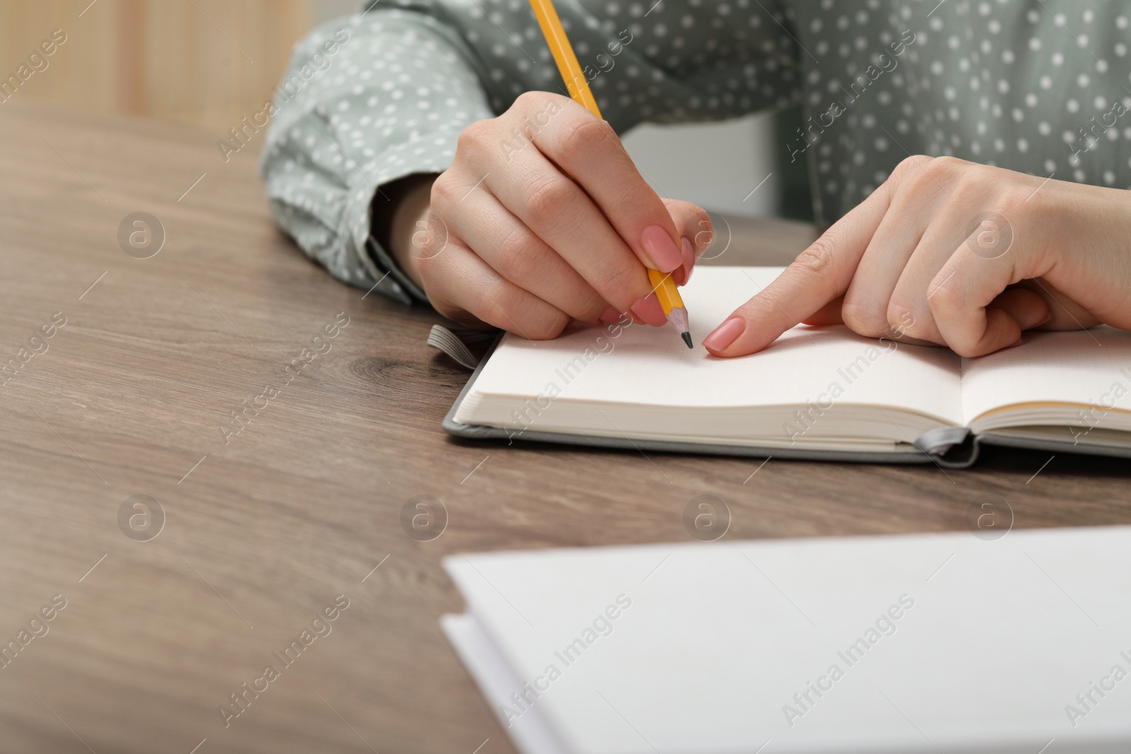 Photo of Woman writing in notebook at wooden table indoors, closeup