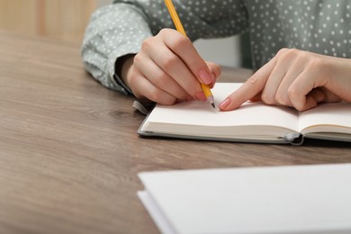 Woman writing in notebook at wooden table indoors, closeup