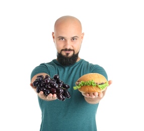 Overweight man with hamburger and grapes on white background