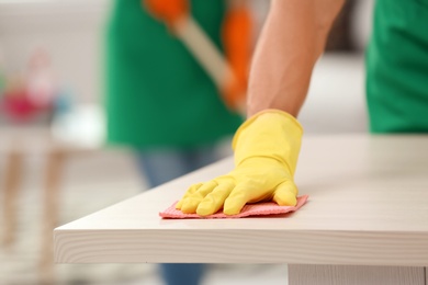 Photo of Man in gloves cleaning table indoors, closeup