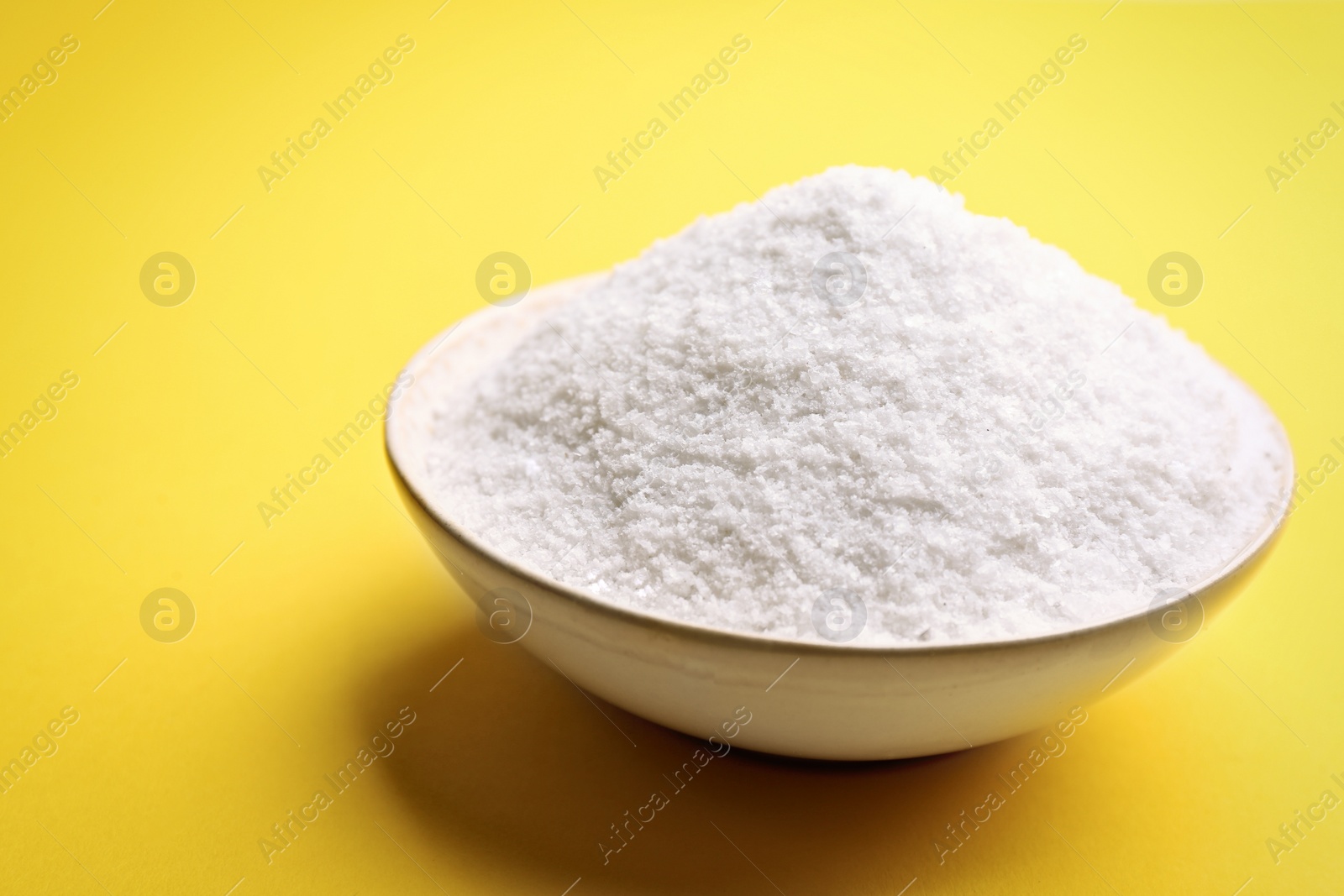 Photo of Bowl with salt on yellow background, closeup