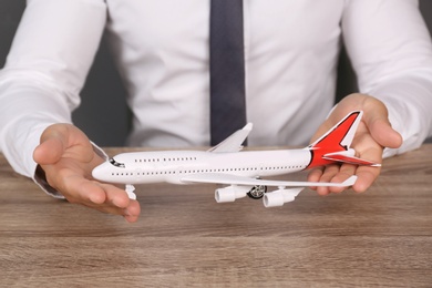 Photo of Insurance agent holding toy plane at table, closeup. Travel safety concept