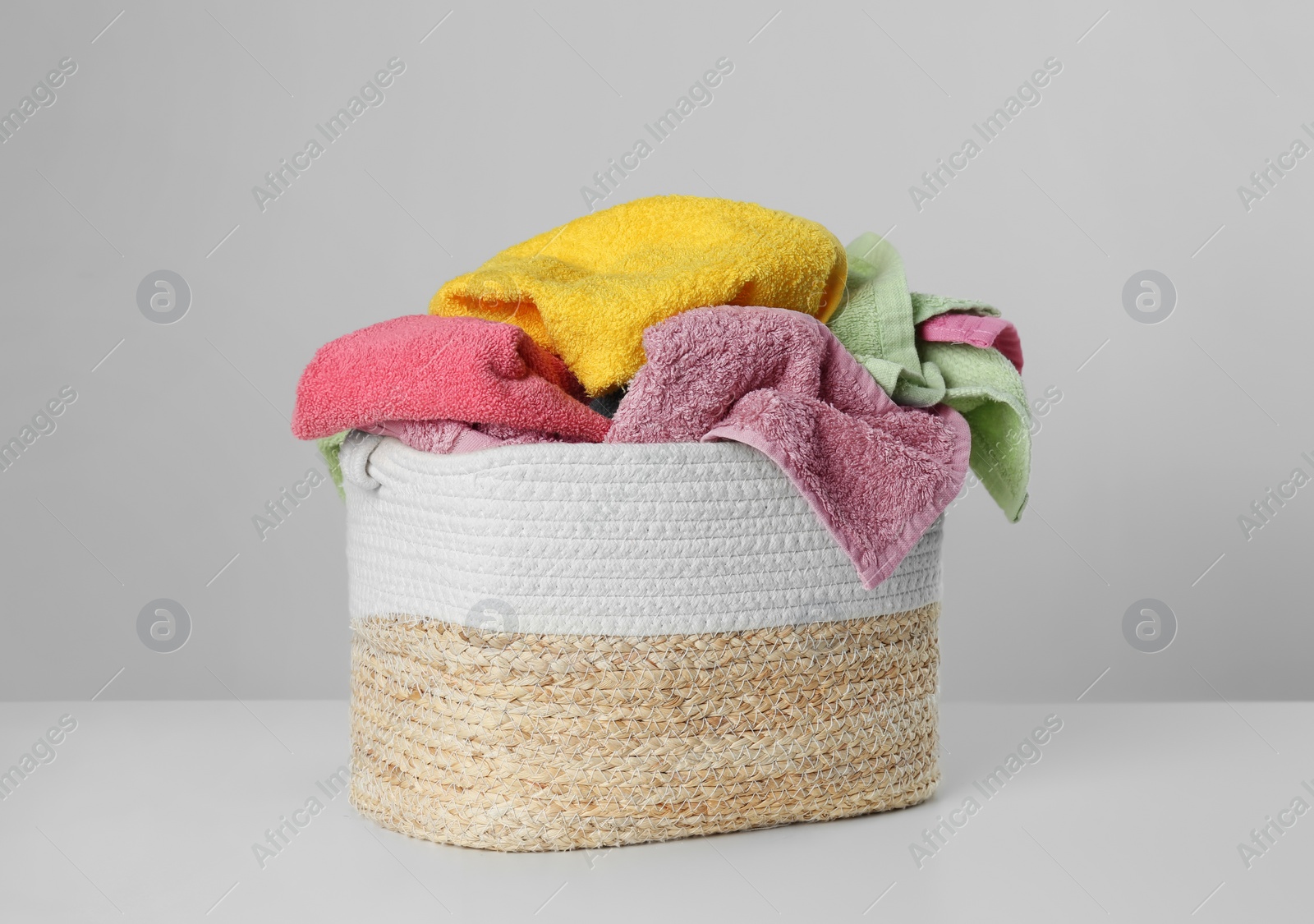 Photo of Wicker laundry basket with towels on light background