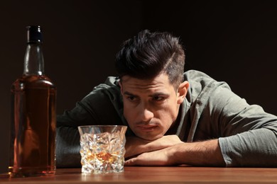 Addicted man and alcoholic drink at wooden table against dark background