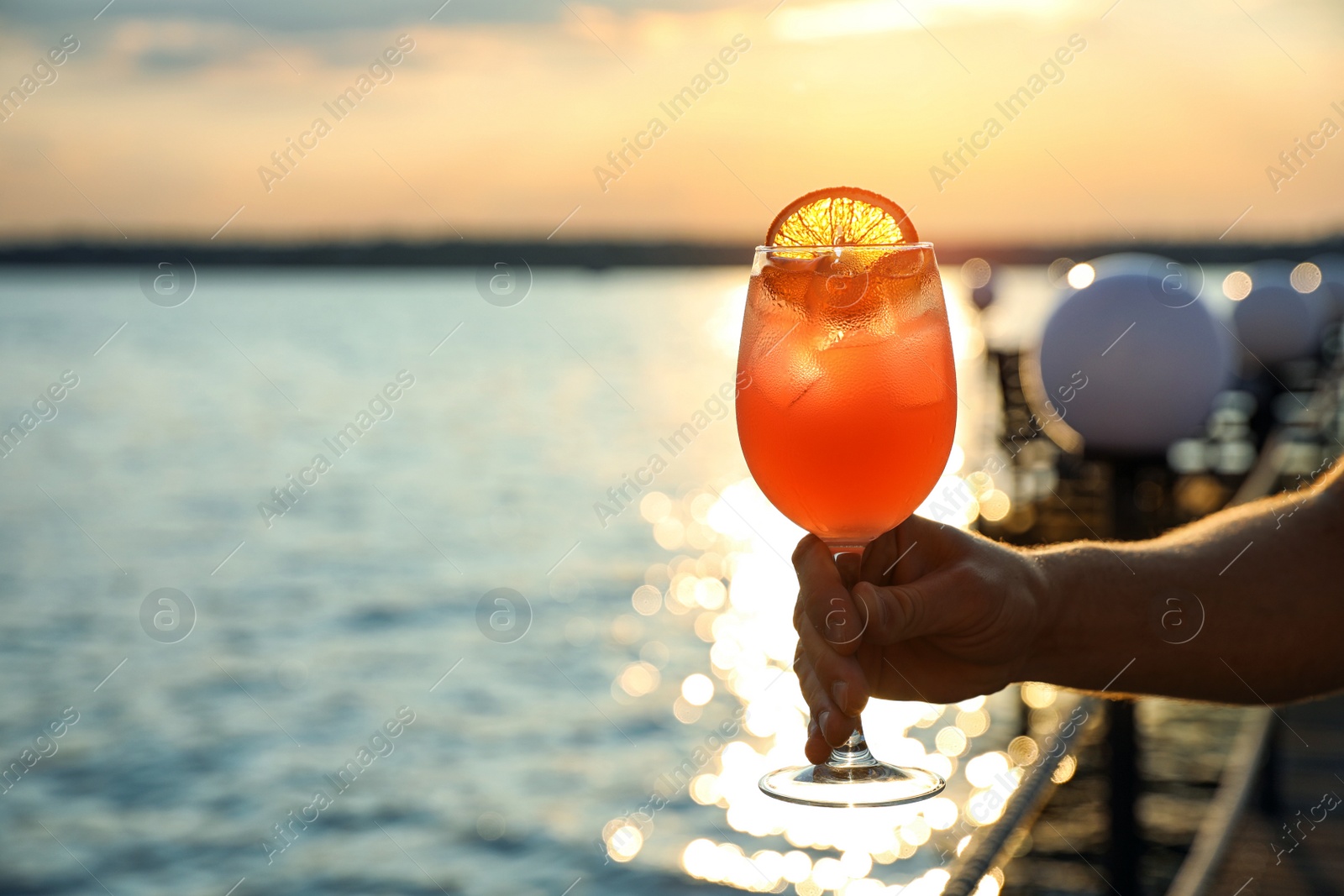 Photo of Man with glass of fresh summer cocktail near water at sunset, closeup. Space for text