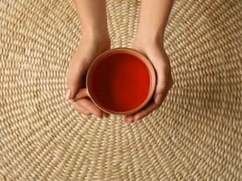 Woman with cup of black tea at wicker table, top view