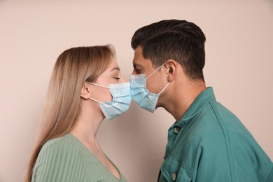 Photo of Couple in medical masks trying to kiss on beige background