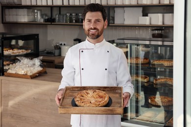 Photo of Professional baker with freshly baked pastry in store