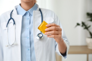 Photo of Female doctor holding condom indoors, closeup. Safe sex concept